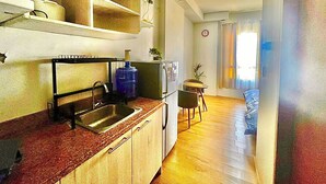 Une cuisine compacte équipée d’un évier, d’un distributeur d’eau et d’un réfrigérateur. Un petit coin repas avec une table et des chaises est également prévu.