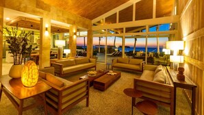 Un hall espacioso con techos altos, ventanas grandes que ofrecen vistas de la puesta de sol y un área de descanso con sofás y mesas.