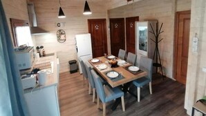 A dining area with a wooden table set for six, surrounded by blue chairs. There are two pendant lights above the table, and a ship's wheel decoration on the wall. - CHALET L'AVENTURE 14km from VANNES (Sulniac)