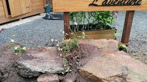 A wooden sign with the text "Chalet L'aventure" in a cursive font, placed on a stone base with a garden bed in the background. - CHALET L'AVENTURE 14km from VANNES (Sulniac)
