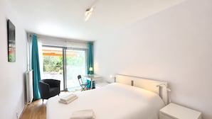 A modern hotel room with a large bed, a desk, a chair, and a view of the outdoors.