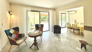 A spacious living area with a round wooden table, two patterned armchairs, a black armchair, and a dining table with chairs.