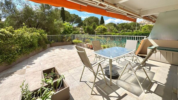 An outdoor patio with a glass table and chairs, surrounded by a white railing and orange awning.