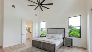 Une chambre avec un grand lit, une table de chevet, un ventilateur de plafond et une fenêtre donnant sur un paysage verdoyant.