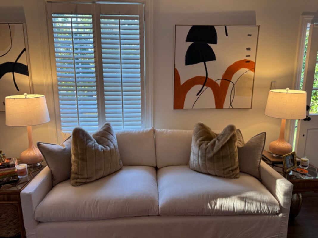 A living room with a beige sofa, two lamps, and abstract wall art.