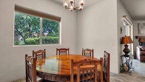 A dining area with a wooden table and chairs, a chandelier, a window with a view of trees, and a lamp on a side table. - Casita Paz at The Tubac Sanctuary (Tubac)