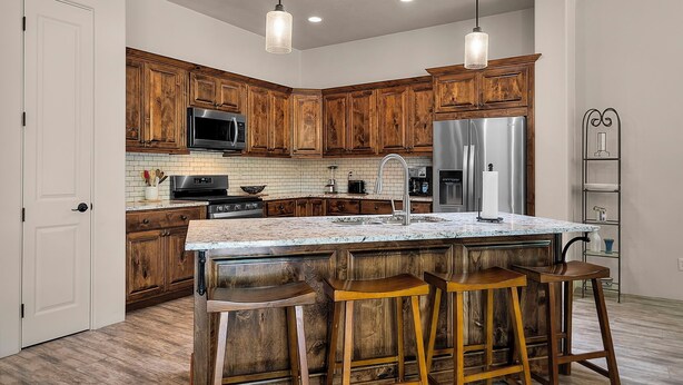 A kitchen with wooden cabinets, a stainless steel refrigerator, a microwave, and a large island with bar stools. - Casita Paz at The Tubac Sanctuary (Tubac)
