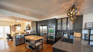 A modern kitchen with dark cabinetry, stainless steel appliances, a central island, and pendant lighting.