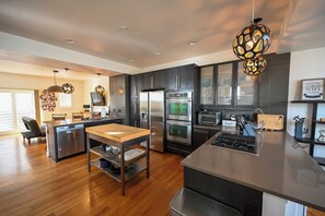 A modern kitchen with dark cabinetry, stainless steel appliances, a central island, and pendant lighting.