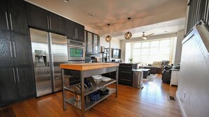 A modern kitchen with dark cabinets, stainless steel appliances, a wooden countertop, and a built-in dishwasher.