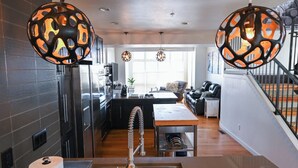 A modern kitchen with a central island, pendant lights, and a view into the living area.