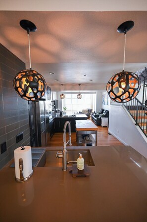 Uma cozinha moderna com ilha central, luminárias pendentes e vista para a sala de estar.