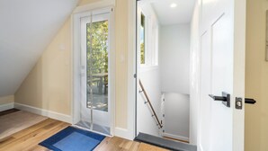 Een kamer met een schuine kap, een houten vloer, een schuifdeur van glas en een deur met een metalen handgreep.