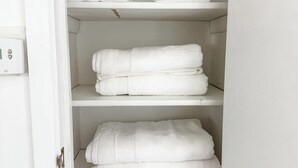A white closet with three shelves, each holding neatly folded white towels.