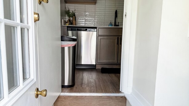 A kitchen with wooden cabinets, a stainless steel dishwasher, and a trash can.