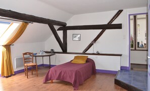 Relax in this loft-style apartment with a central bed, wooden chair, and small table for a peaceful retreat.