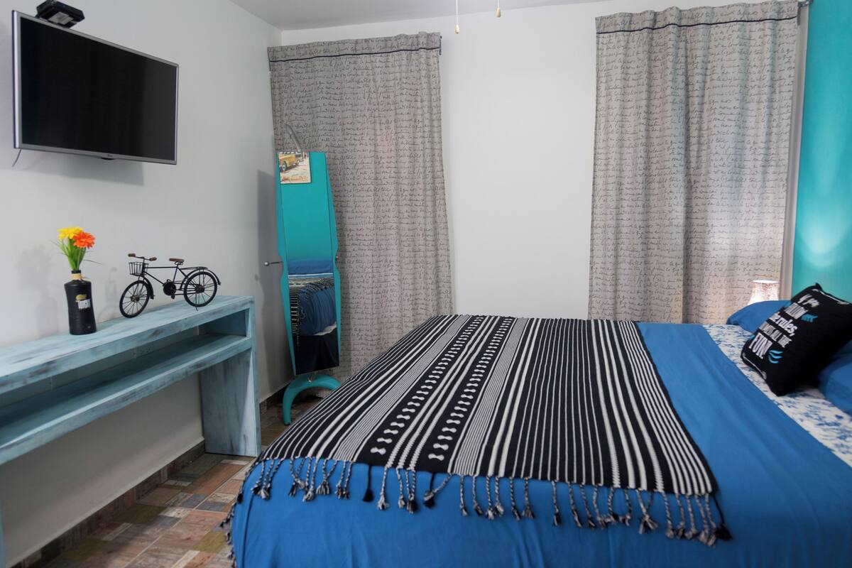 Une chambre à coucher avec un lit, une télévision, une étagère sur laquelle se trouve un vélo, et un miroir.