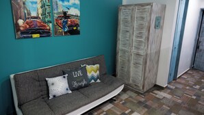 Une pièce aux murs de couleur turquoise, avec un canapé gris orné de coussins à motifs et une armoire en bois.