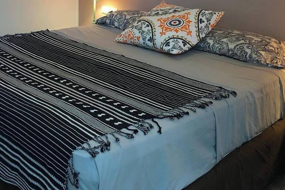 Une chambre à coucher avec un lit, des coussins à motifs, une lampe fixée au mur et un tableau.