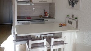 A compact kitchen with white cabinetry, a microwave, a sink, and a small countertop area. There are three white chairs with cushions. - 5 minutes from the La Legette chairlift, Studio-Cabin 21m² Les Saisies (Hauteluce)