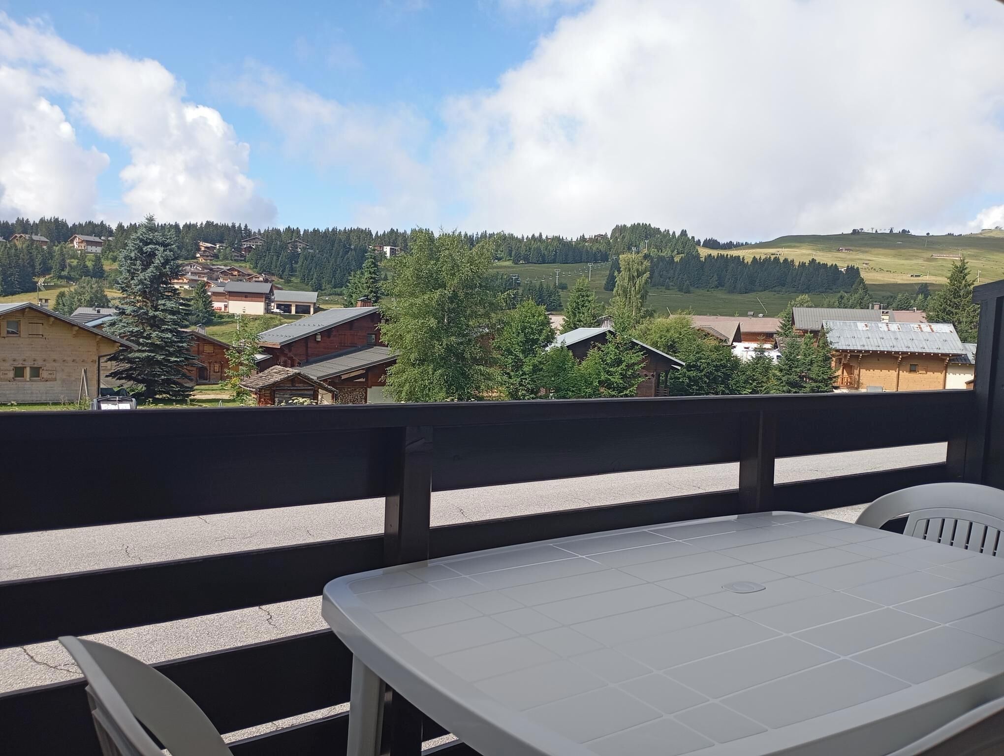 Un balcón con mesa y sillas que da a un pueblo con casas y árboles.