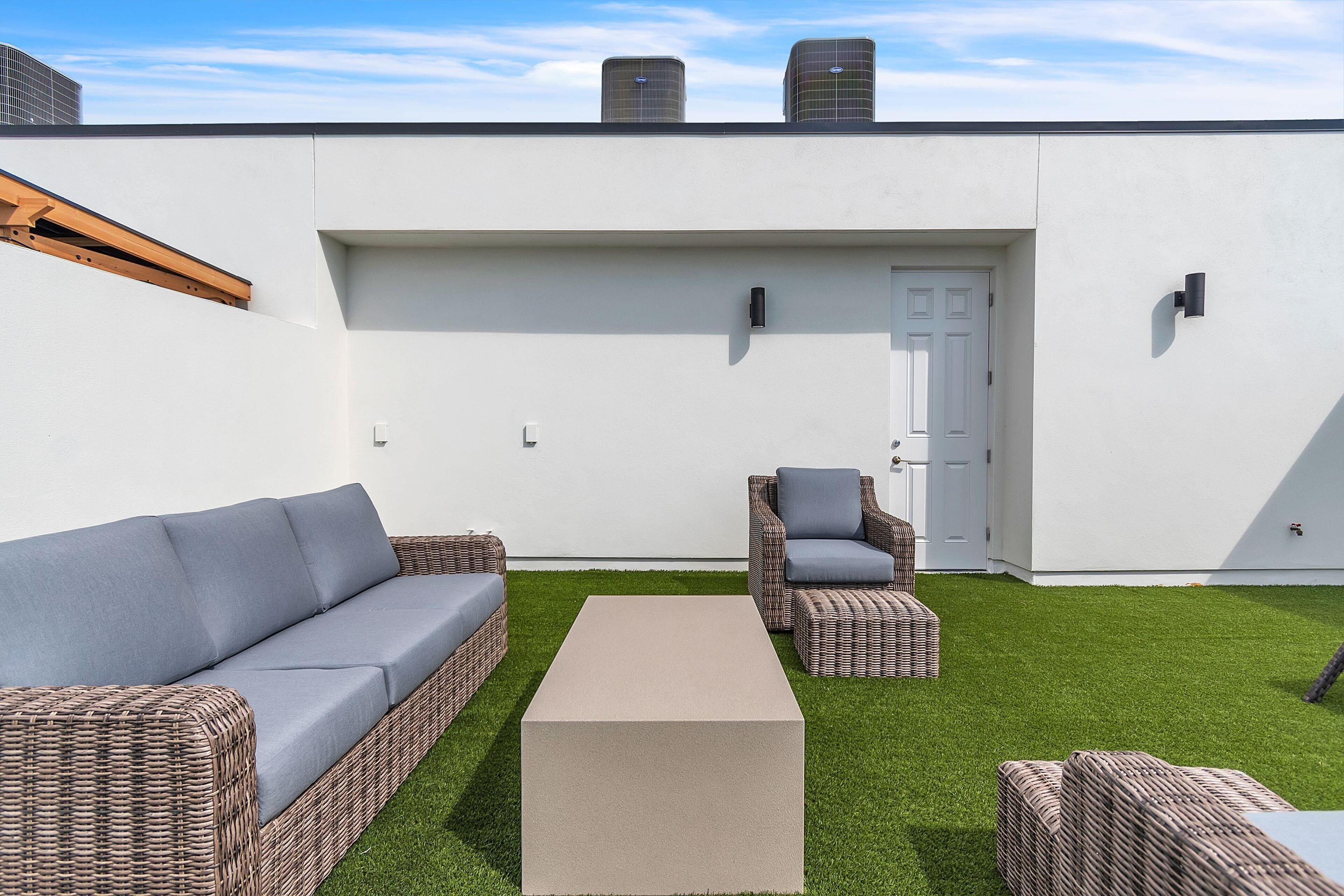 En moderne udendørs terrasse med en hvid væg, en dør og to fletsofaer med hynder.
