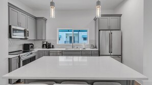 A modern kitchen with a large island, stainless steel appliances, and pendant lighting. - Azul Townhomes A3 - Sunrise (Madeira Beach)