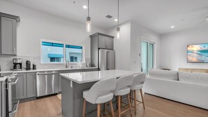 A modern kitchen with grey cabinets, stainless steel appliances, and a central island with bar stools. - Azul Townhomes A3 - Sunrise (Madeira Beach)