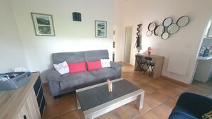 A living room with a grey sofa, red cushions, a coffee table, and a dining area with a small table and chairs.