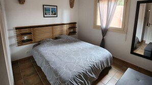 A bedroom with a bed, a bench, a window with curtains, and wall decorations.