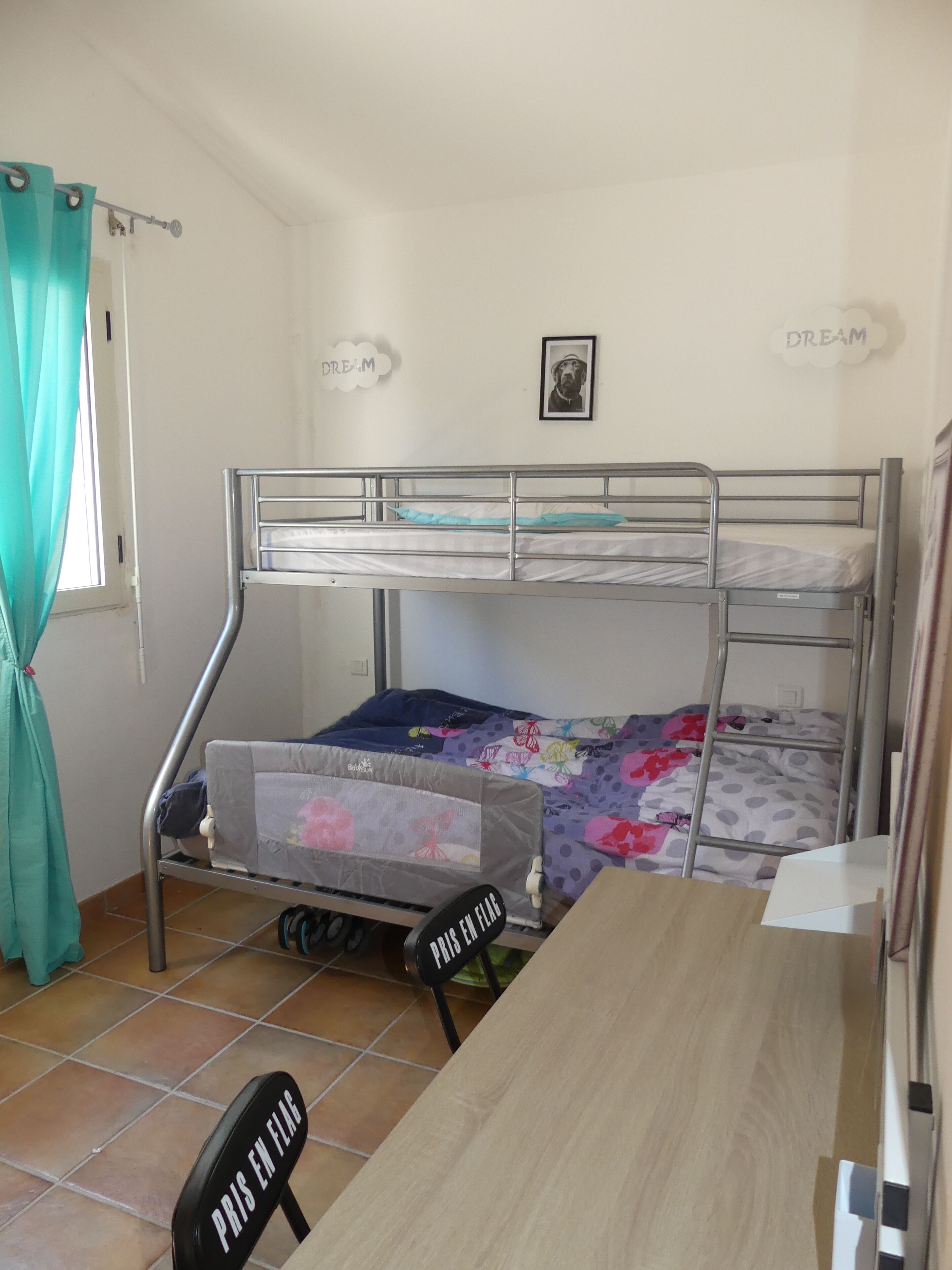 Een studentenkamer met stapelbedden, een bureau, een stoel en een raam met gordijnen.