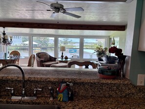 A kitchen with granite countertops, a ceiling fan, and a view of a body of water through large windows. - Salty Kayaker's Red Fish Cove Cottage (Ozello)