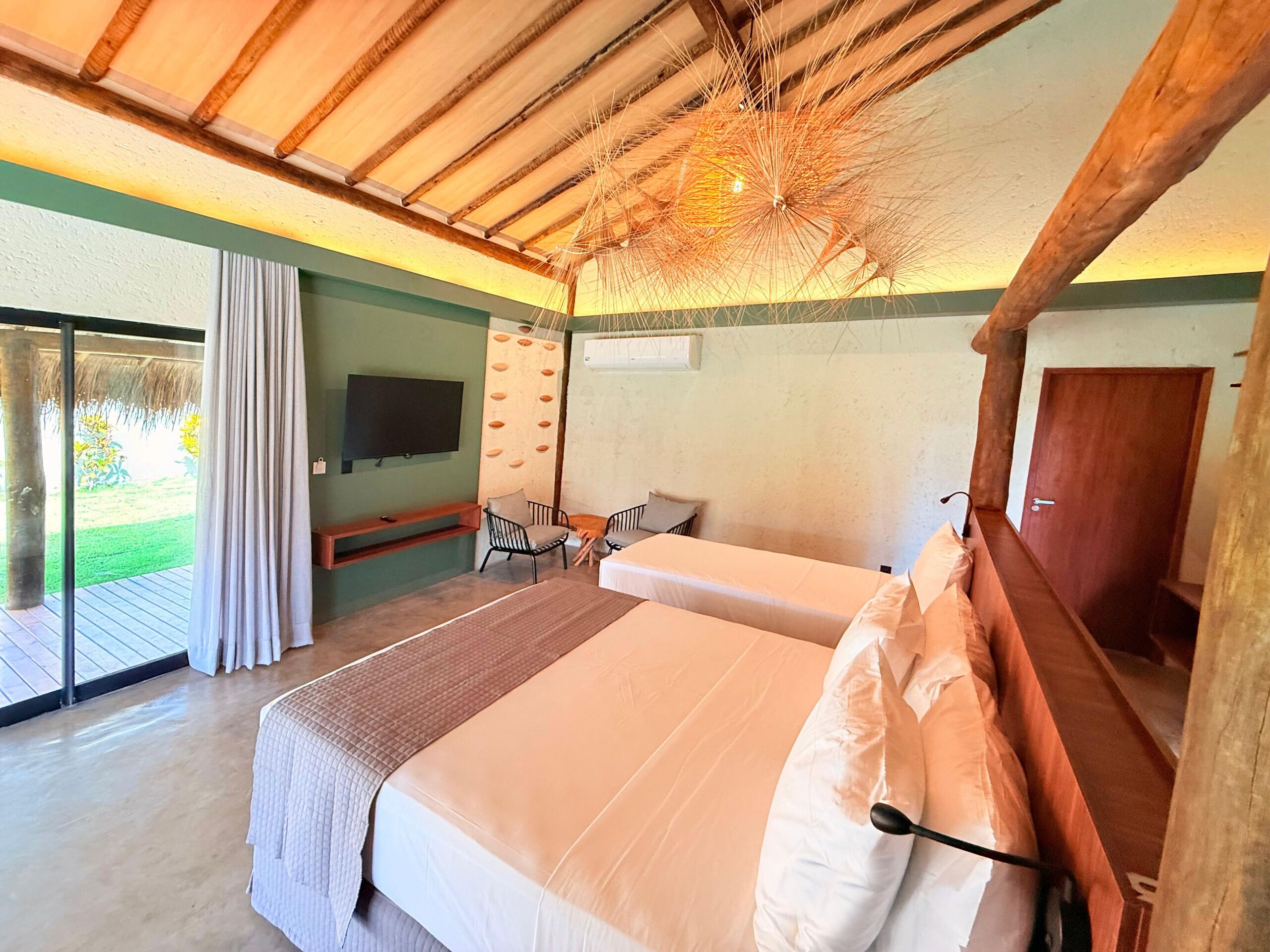 A bedroom with two beds, a TV, a seating area, and a view of the outdoors.