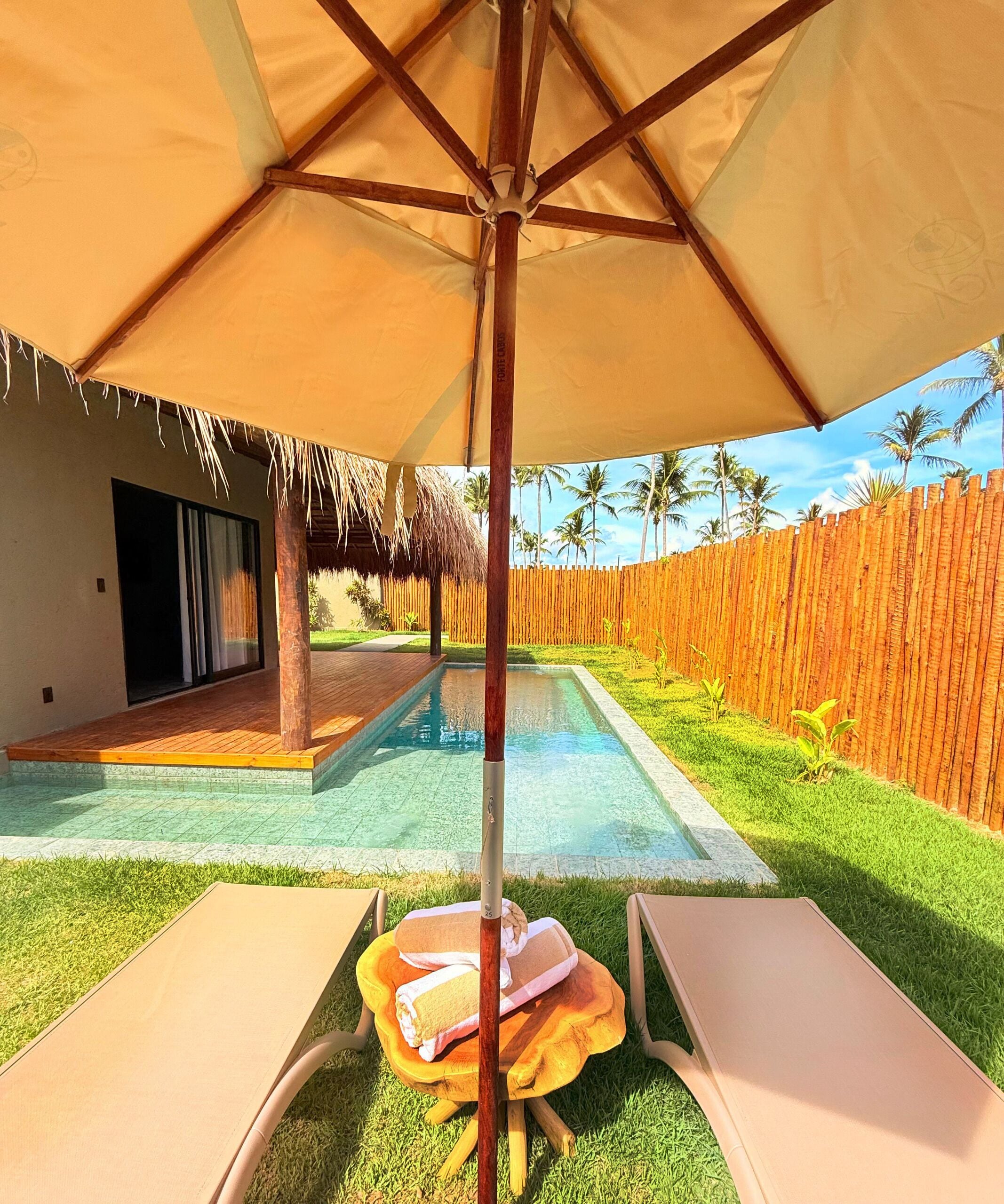 A pool area with a wooden deck, lounge chairs, and a thatched-roof structure.
