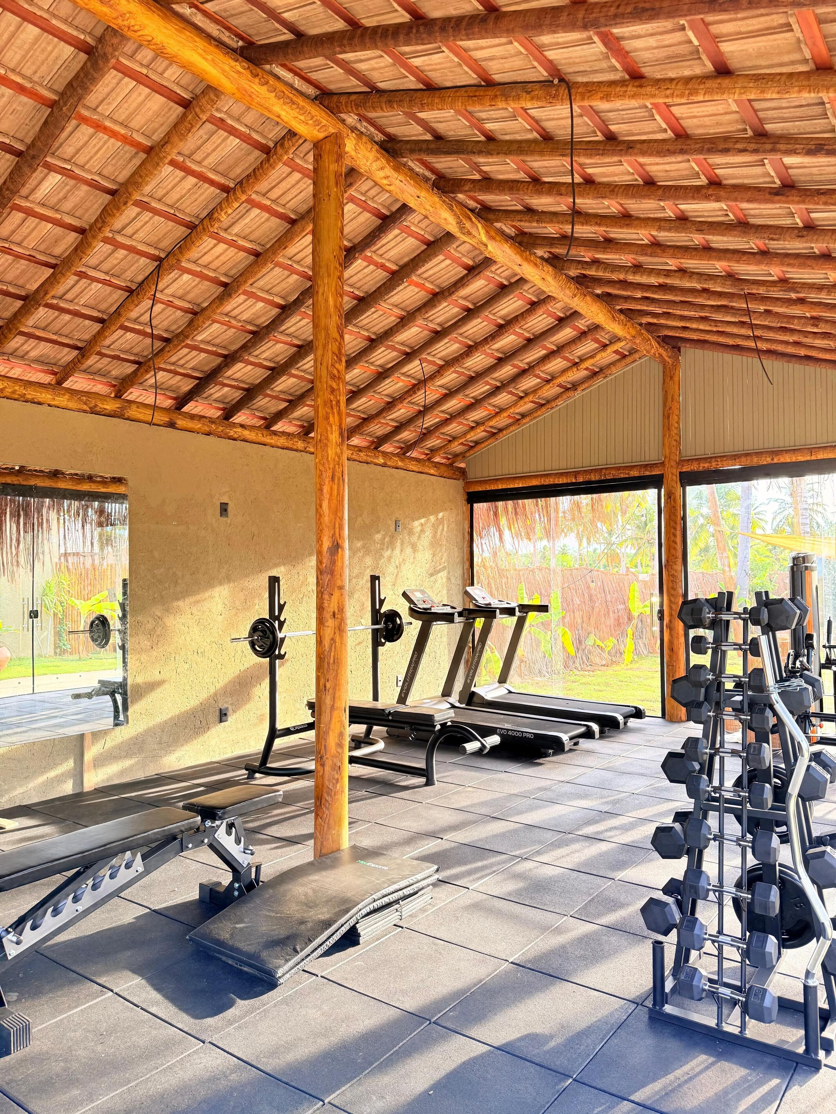 A covered gym with exercise equipment, including treadmills, a squat rack, and a dumbbell rack.