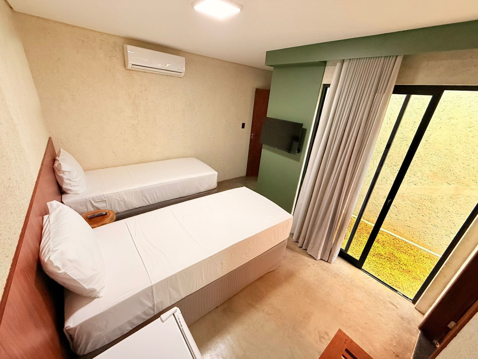A hotel room with two single beds, a TV, and a sliding glass door to the outside.