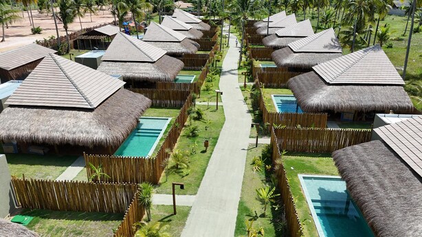 Un resort con bungalows de techo de paja dispuestos en filas, cada uno con piscina privada.