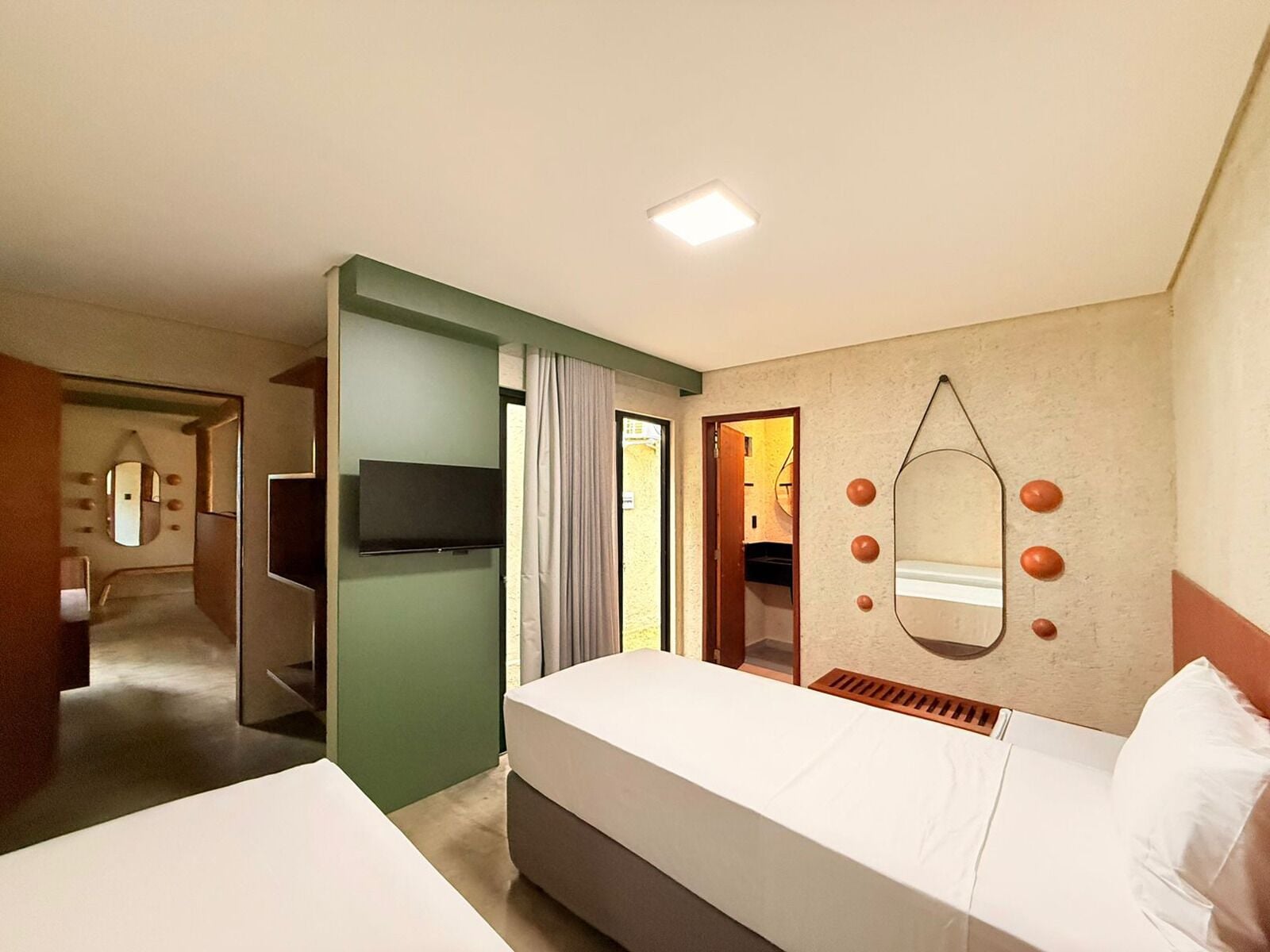 A hotel room with a bed, a TV, a mirror, and a door leading to a bathroom.