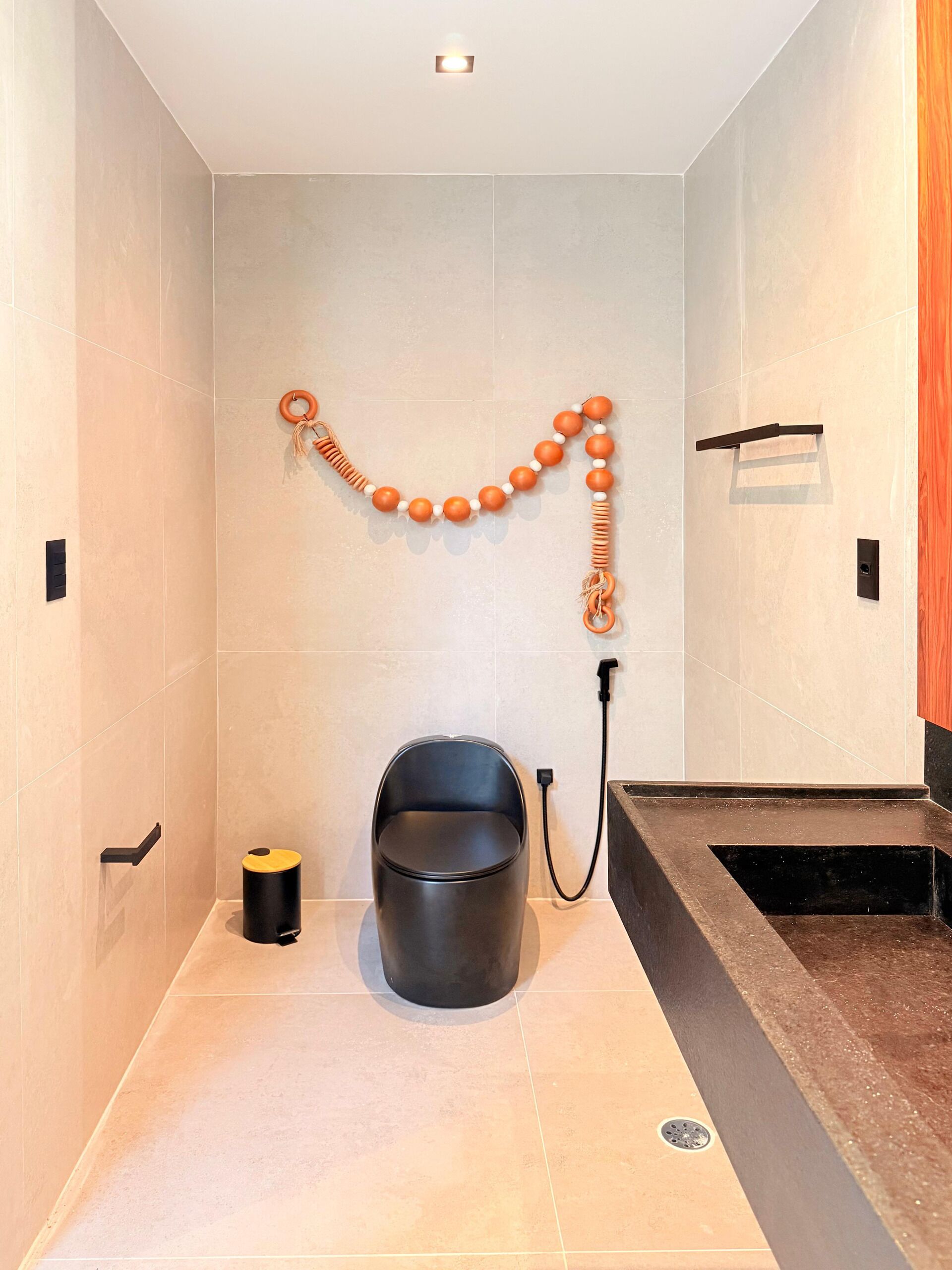 A modern bathroom with a black bucket, a towel rack, and a shower area.