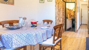 A dining area with a table set for four, wooden chairs, a kitchen visible through an open doorway, and a wall with framed pictures. - Le Grand Som - Proche Station de ski (Saint-Pierre-de-Chartreuse)