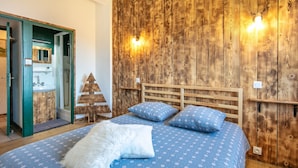 A bedroom with a wooden headboard, a bed with a blue patterned bedspread, two pillows, and a fluffy white throw. - Le Grand Som - Proche Station de ski (Saint-Pierre-de-Chartreuse)