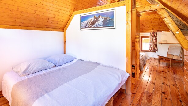 Habitación con paneles de madera, una cama, un cuadro en la pared y un ventanal con cortinas.