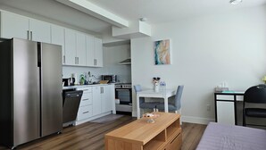 A modern kitchen with stainless steel appliances, a dining area with a wooden table, and a small workspace with a chair. - Private south-facing suite with a full bathroom and fully equipped kitchen. (Coquitlam)