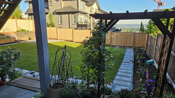 A backyard with a wooden pergola, a stone pathway, and a variety of potted plants. - Private south-facing suite with a full bathroom and fully equipped kitchen. (Coquitlam)