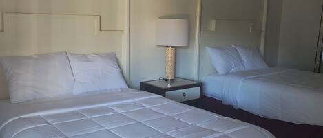 A hotel room with two beds, a nightstand with a lamp, and a ceiling light fixture.