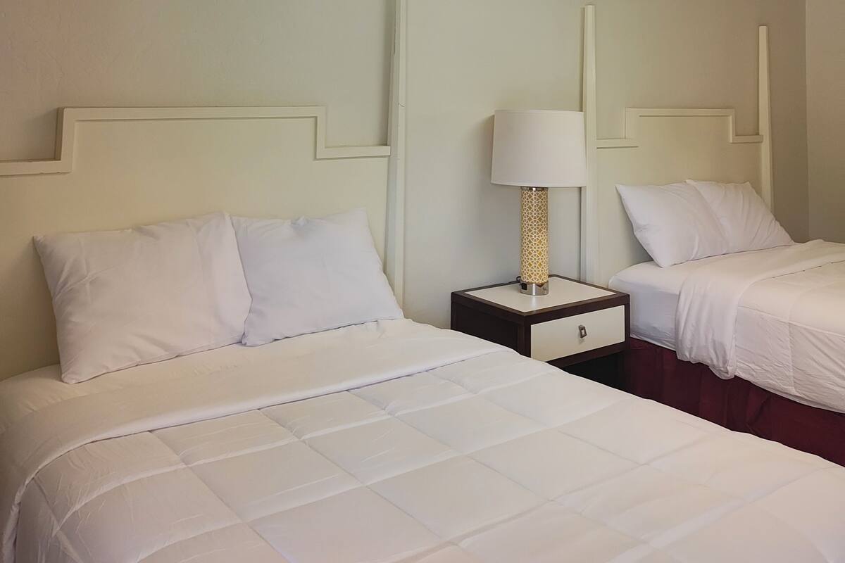 A hotel room with two beds, a nightstand with a lamp, and a ceiling light fixture.