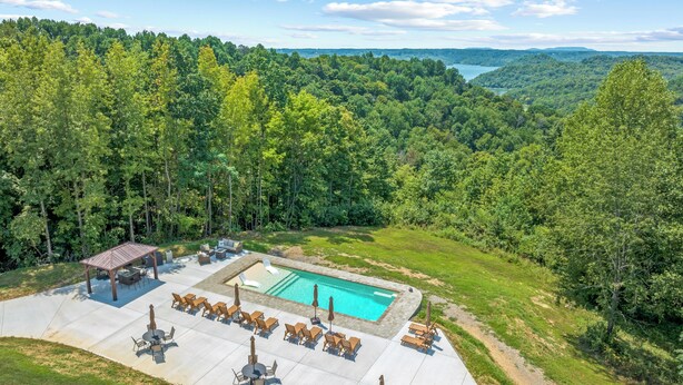 An outdoor pool area with lounge chairs and a gazebo, surrounded by a forested landscape.