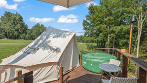 A tent on a wooden deck with a green inflatable hot tub and two white chairs.