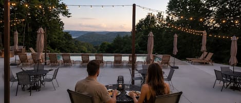 An outdoor patio with tables and chairs, string lights, and umbrellas.