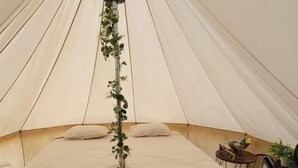 A tent with two beds, a small table with a 'Welcome' sign, and a refrigerator.